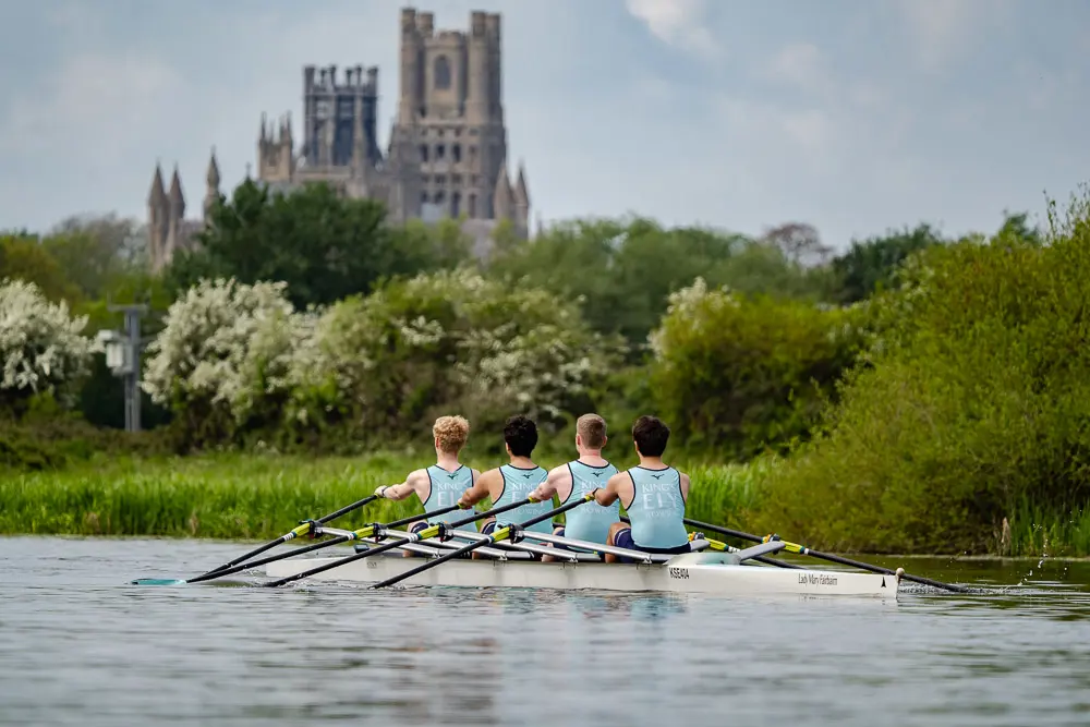 Kings Ely Senior Rowing team rowing on the River Ouse with Ely Cathedral in the background 